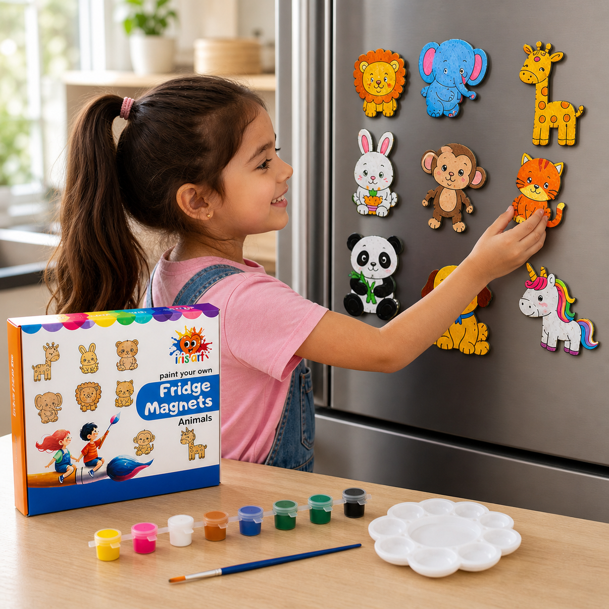 Child placing painted animal fridge magnets on a fridge, with the Fridge Magnets kit box and paints